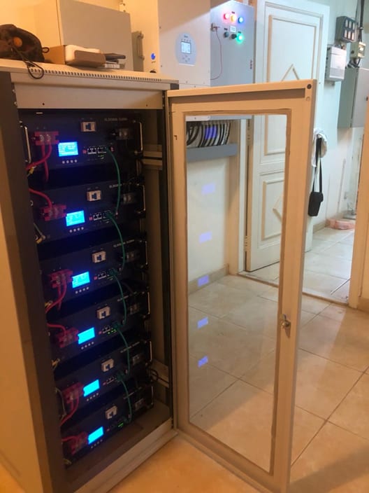 Open battery cabinet holding six stacked lithium battery modules, each with a lit status display