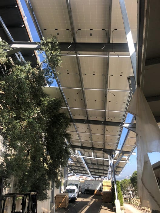 Underside of a photovoltaic canopy over a service road, showing the steel frame and cabling between panels